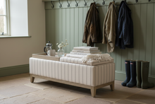 Load image into Gallery viewer, A cream tufted upholstered storage bench with a light wood frame and legs, styled in a bedroom setting with a wooden tray, books, and a small vase on top.
