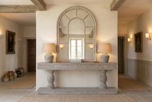 Load image into Gallery viewer, A rustic gray console table with turned legs stands against a beige wall, decorated with two white vases of pink hydrangeas and a framed landscape painting above.
